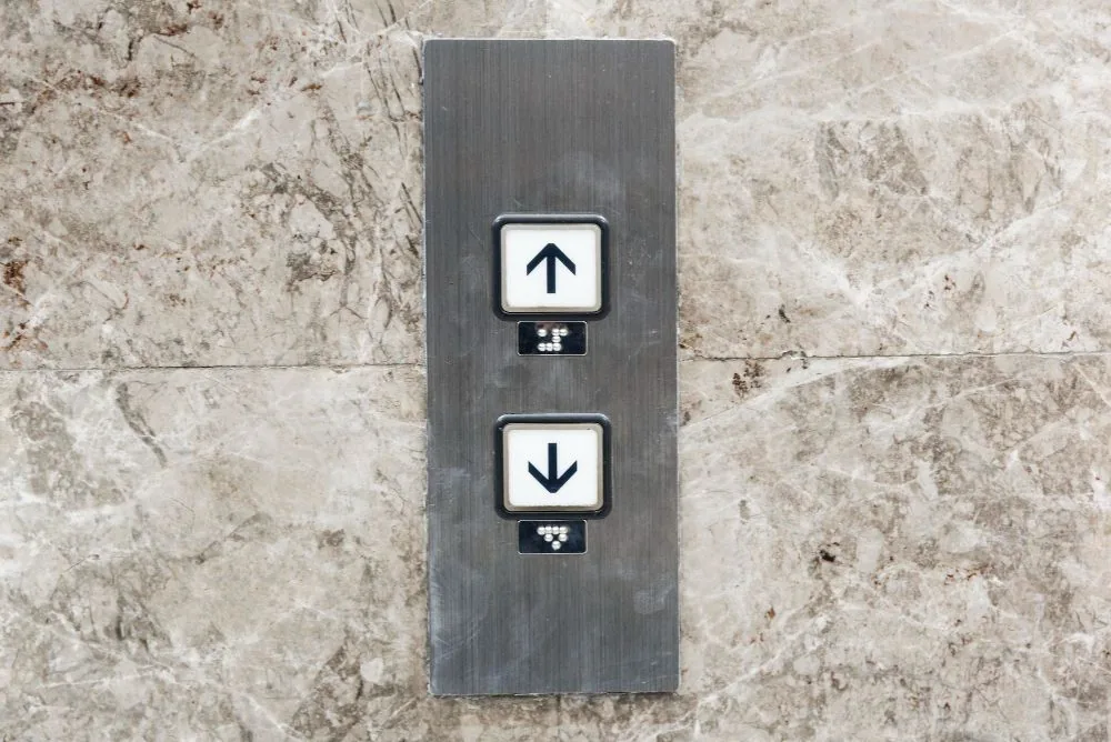 Lift call buttons with braille on a marble wall
